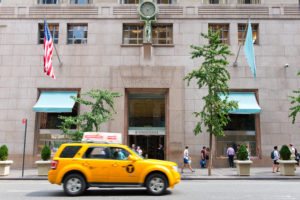Yellow cab driving past the front facade of Tiffany and Co, New York, a famous breakfast venue and retailer in silverware and jewellery