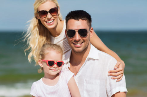 family, vacation, adoption and people concept - happy man, woman and little girl in sunglasses on summer beach